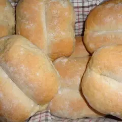 Świeżo upieczone bułki pszenno żytnie, lekko oprószone mąką, ułożone w koszyku.