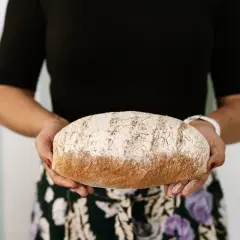 Kobieta trzyma bochenek chleba razowego. Zastanawiasz się, ile kcal ma kromka chleba razowego? Ten pyszny chleb może być częścią zdrowej diety.