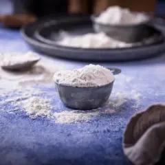 Mąka w miarkach na niebieskim blacie. Zastanawiasz się, ile szklanek mąki jest w kilogramie?