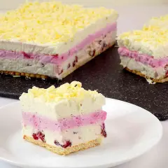 Lekkie, owocowe ciasto na lato z warstwami bitej śmietany, różowego musu i owoców, posypane wiórkami białej czekolady. Idealne na upalne dni.