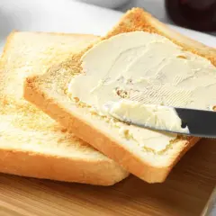 Na desce leżą dwa tosty. Na jednym z nich nóż rozsmarowuje masło. Ile gram ma kromka chleba tostowego?