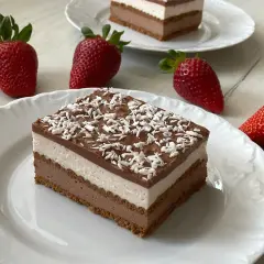Pyszne ciasto z mascarpone bez pieczenia, warstwowe, z polewą czekoladową i wiórkami kokosowymi. Obok świeże truskawki.