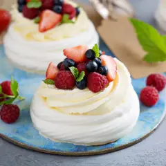 Beza pavlova z mascarpone, udekorowana malinami, borówkami i truskawkami. Letni deser na błękitnym talerzu.