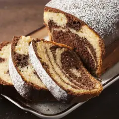 Pyszne ciasto zebra w keksówce, posypane cukrem pudrem, z kilkoma pokrojonymi kawałkami.
