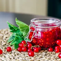 Słoik pełen domowego dżemu z czerwonej porzeczki, otoczony świeżymi owocami i liśćmi.