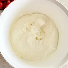 Gładki, puszysty krem z serka mascarpone w białej misie, gotowy do deseru. Obok miski widać świeże truskawki.