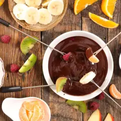 Czekolada do fontanny z owocami: maliny, kiwi, banany, pomarańcze na drewnianym stole.
