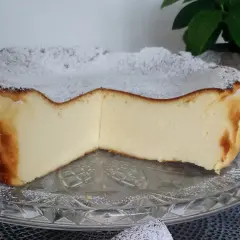 Puszyste ciasto z mlekiem skondensowanym, oprószone cukrem pudrem, prezentuje się apetycznie na szklanej paterze.
