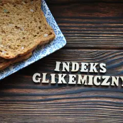 Plasterki chleba pełnoziarnistego na talerzyku z niebieskim wzorem. Obok drewniane litery układają się w napis "INDEKS GLIKEMICZNY".