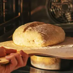 Chleb na desce wychodzi z piekarnika. Złocista skórka i lekko oprószony mąką wierzch sugerują, że to dobry moment, by sprawdzić, jak sprawdzić czy chleb jest upieczony.