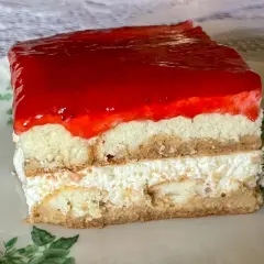 Pyszne ciasto z biszkoptów z kremem i galaretką truskawkową, podane na talerzyku z zielonymi listkami.