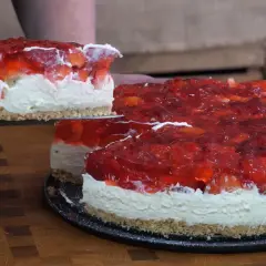 Krojony tort z galaretką truskawkową i bitą śmietaną na spodzie z ciastek.