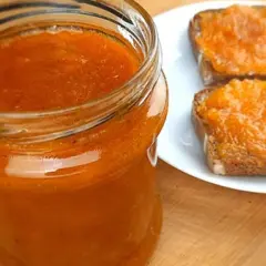 Słoik pełen domowego dżemu z brzoskwini obok dwóch tostów posmarowanych tym pysznym dżemem.