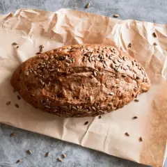 Chleb z mąki chlebowej, posypany słonecznikiem, leży na papierze.
