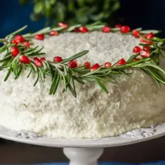 Białe ciasto na Boże Narodzenie, udekorowane gałązkami rozmarynu i nasionami granatu, wygląda jak zimowa ozdoba.