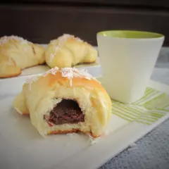 Pyszne rogaliki drożdżowe z budyniem, posypane wiórkami kokosowymi, obok filiżanki.