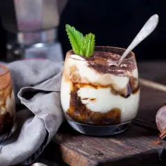 Pyszne tiramisu w pucharkach, udekorowane listkiem mięty i posypane kakao. Idealne na deser.