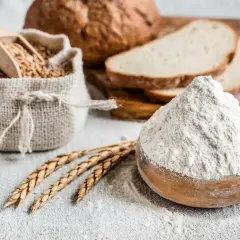 Mąka żytnia w misce, ziarna w worku i kromki chleba. Czy mąka żytnia jest zdrowa? Tak, to podstawa zdrowego pieczywa.