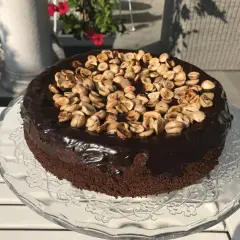 Czekoladowy tort z polewą i orzechami na szklanej paterze.