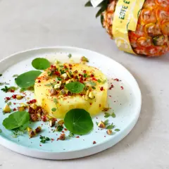 Okrągły kawałek ananasa, posypany pistacjami i przyprawami, na talerzu z liśćmi nasturcji. Czy mrożony ananas nadaje się do galaretki?