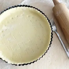 Surowe ciasto kruche w formie do tarty, widelec i wałek. Czy do kruchego ciasta daje się proszek do pieczenia?