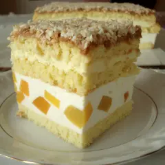 Pyszne ciasto z brzoskwiniami i kremem, posypane wiórkami kokosowymi. Wygląda jak bogini Wenus na talerzu.