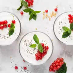 Trzy pucharki z jogurtem naturalnym, udekorowane porzeczkami i miętą. Zastanawiasz się, ile cukru ma jogurt naturalny? Ten jest pyszny i zdrowy!
