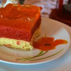 Kawałek ciasta z warstwami biszkoptu, musu truskawkowego i galaretki na talerzyku z makami.