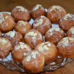 Pyszne pączki z adwokatem, polane lukrem i posypane płatkami migdałów, ułożone na szklanej paterze.