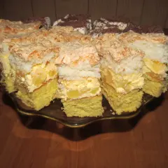 Pyszne ciasto z ananasem i kokosem, z bezą i kremem, pokrojone na kawałki na paterze.