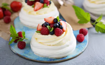 Beza pavlova z mascarpone, udekorowana malinami, borówkami i truskawkami. Letni deser na błękitnym talerzu.