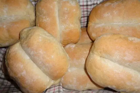 Świeżo upieczone bułki pszenno żytnie, lekko oprószone mąką, ułożone w koszyku.