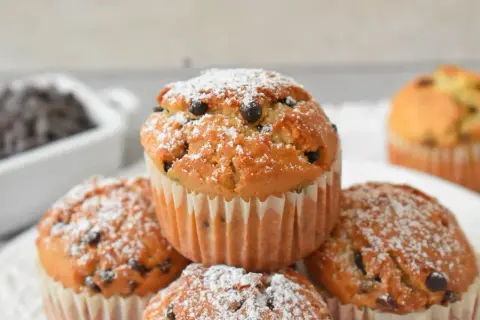 Pyszne muffinki z kawałkami czekolady, posypane cukrem pudrem, kuszą swoim wyglądem. Idealne na deser!