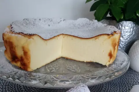 Puszyste ciasto z mlekiem skondensowanym, oprószone cukrem pudrem, prezentuje się apetycznie na szklanej paterze.