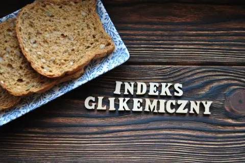 Plasterki chleba pełnoziarnistego na talerzyku z niebieskim wzorem. Obok drewniane litery układają się w napis "INDEKS GLIKEMICZNY".