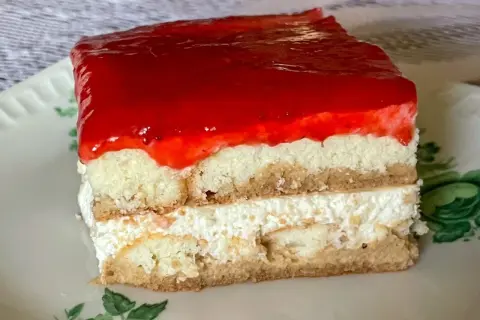 Pyszne ciasto z biszkoptów z kremem i galaretką truskawkową, podane na talerzyku z zielonymi listkami.
