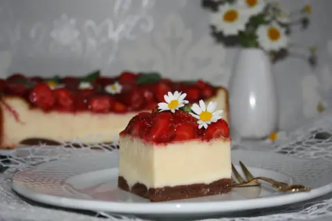 Pyszny sernik z truskawkami, udekorowany świeżymi kwiatkami, kusi swoim wyglądem.