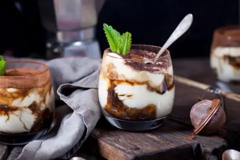 Pyszne tiramisu w pucharkach, udekorowane listkiem mięty i posypane kakao. Idealne na deser.