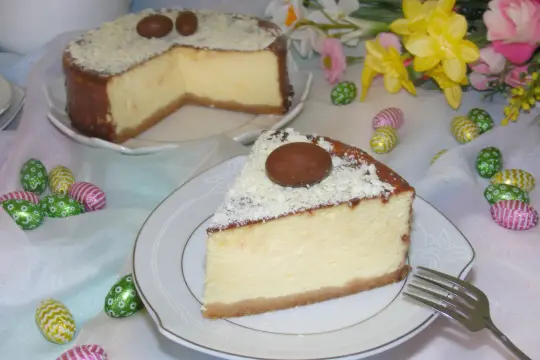 Pyszny sernik z mascarpone i białym serem, ozdobiony czekoladowymi jajeczkami i wiórkami białej czekolady, idealny na święta.