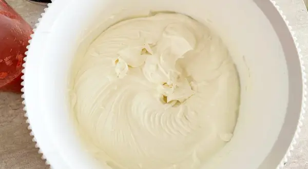 Gładki, puszysty krem z serka mascarpone w białej misie, gotowy do deseru. Obok miski widać świeże truskawki.