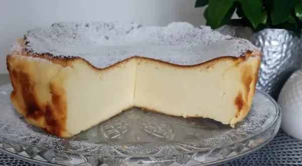 Puszyste ciasto z mlekiem skondensowanym, oprószone cukrem pudrem, prezentuje się apetycznie na szklanej paterze.