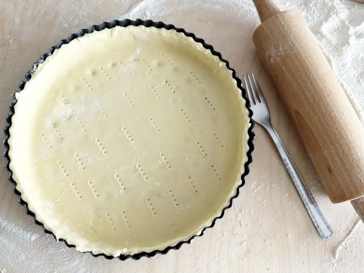 Surowe ciasto kruche w formie do tarty, widelec i wałek. Czy do kruchego ciasta daje się proszek do pieczenia?