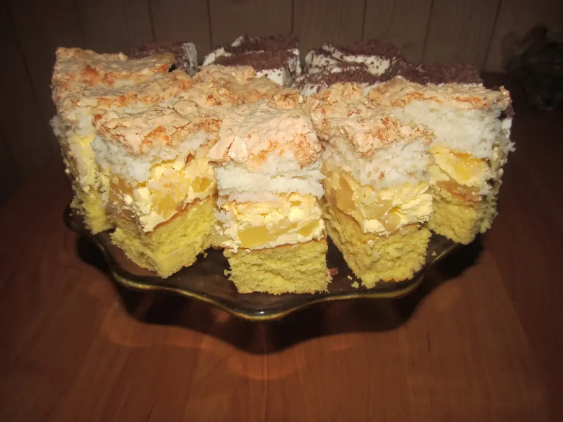 Pyszne ciasto z ananasem i kokosem, z bezą i kremem, pokrojone na kawałki na paterze.