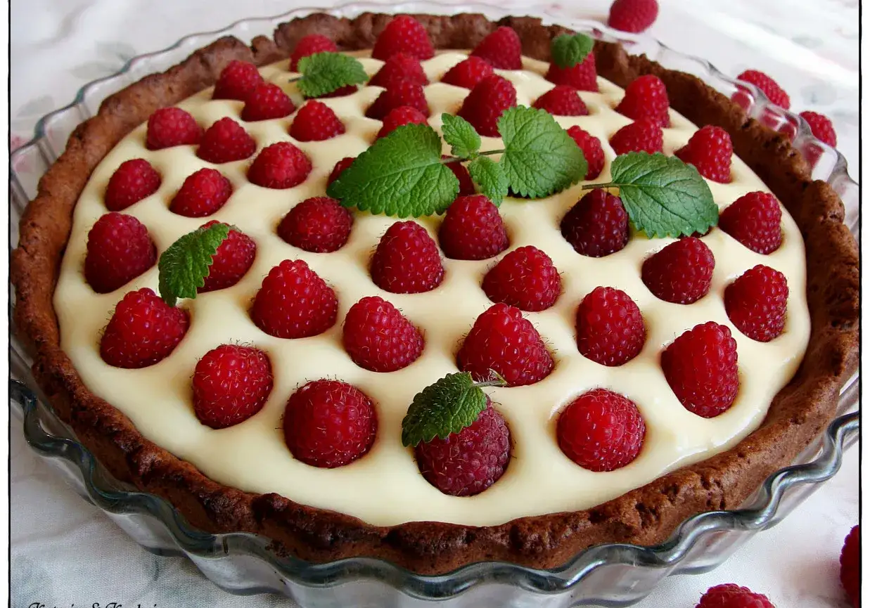 Pyszna tarta z malinami i kremem mascarpone, ozdobiona listkami mięty. Biała czekolada dodaje jej słodyczy.