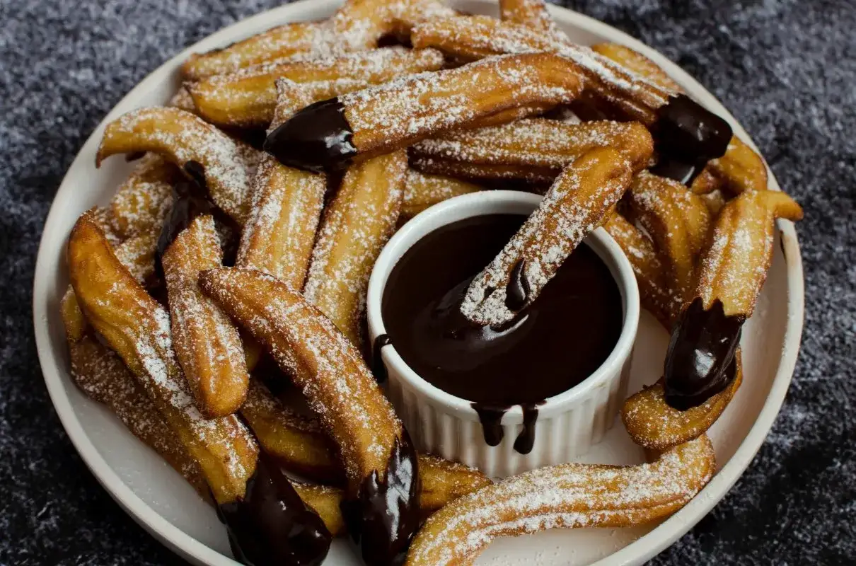 Churros posypane cukrem pudrem, zanurzane w gorącej czekoladzie. Idealny przepis na churros dla każdego łasucha!