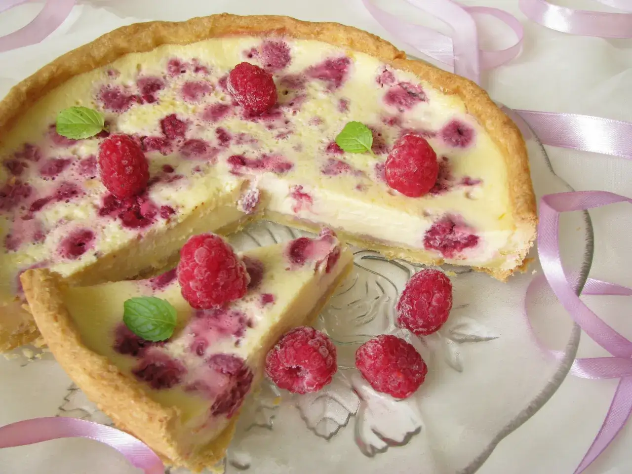 Tarta z malinami i mascarpone, ozdobiona świeżymi malinami i listkami mięty, wygląda apetycznie. Biała czekolada subtelnie podkreśla smak.