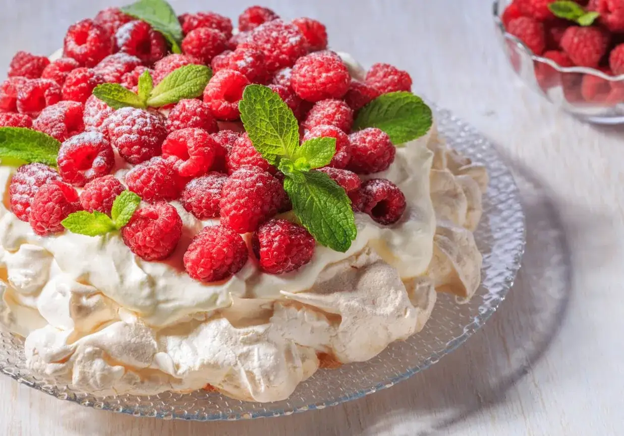 Beza Pavlova z mascarpone, obficie udekorowana malinami i listkami mięty, wygląda jak letni deser marzeń.