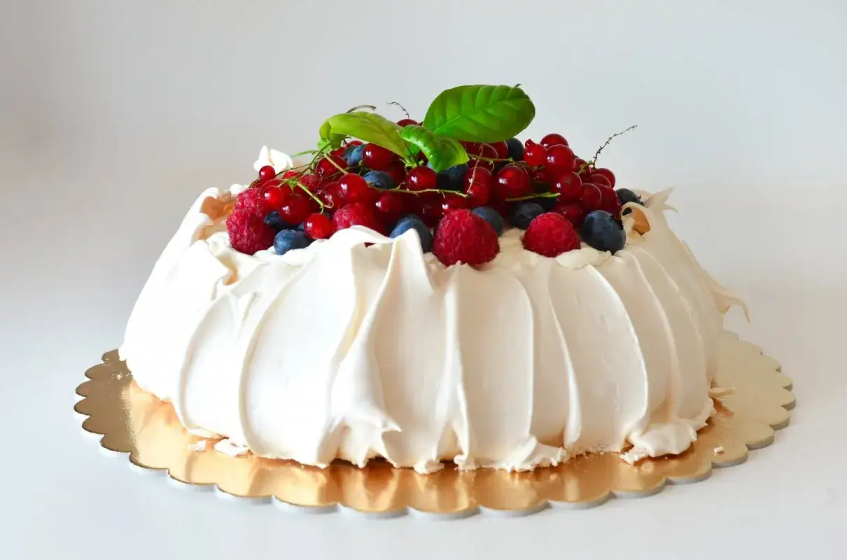 Beza Pavlova z mascarpone, udekorowana świeżymi malinami, borówkami i porzeczkami, wygląda apetycznie.