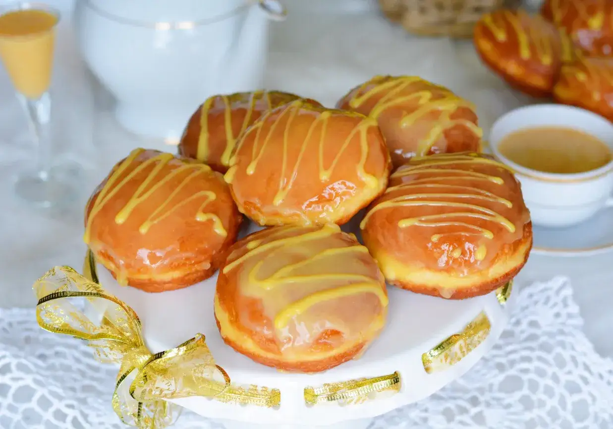 Pyszne pączki z adwokatem, polane lukrem i udekorowane złotą wstążką, czekają na degustację.