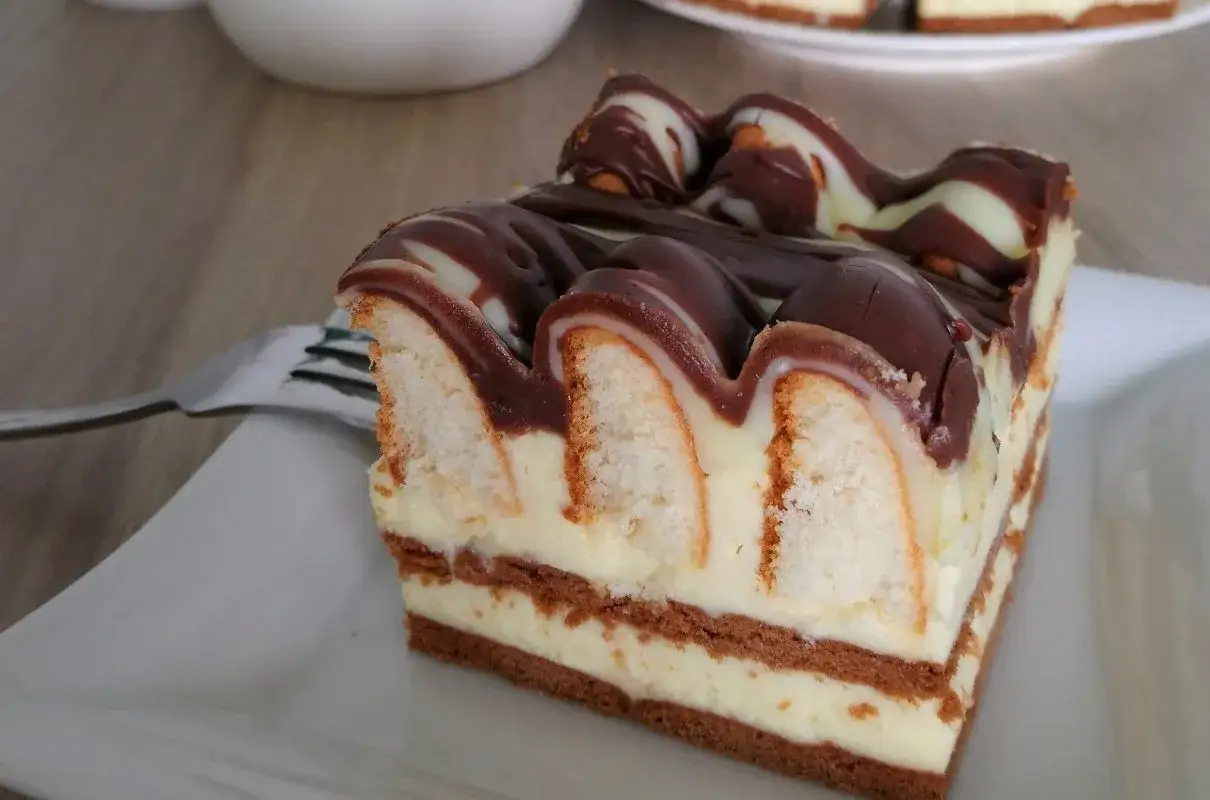 Pyszne ciasto góra lodowa bez pieczenia, przełożone kremem i biszkoptami, polane czekoladą.